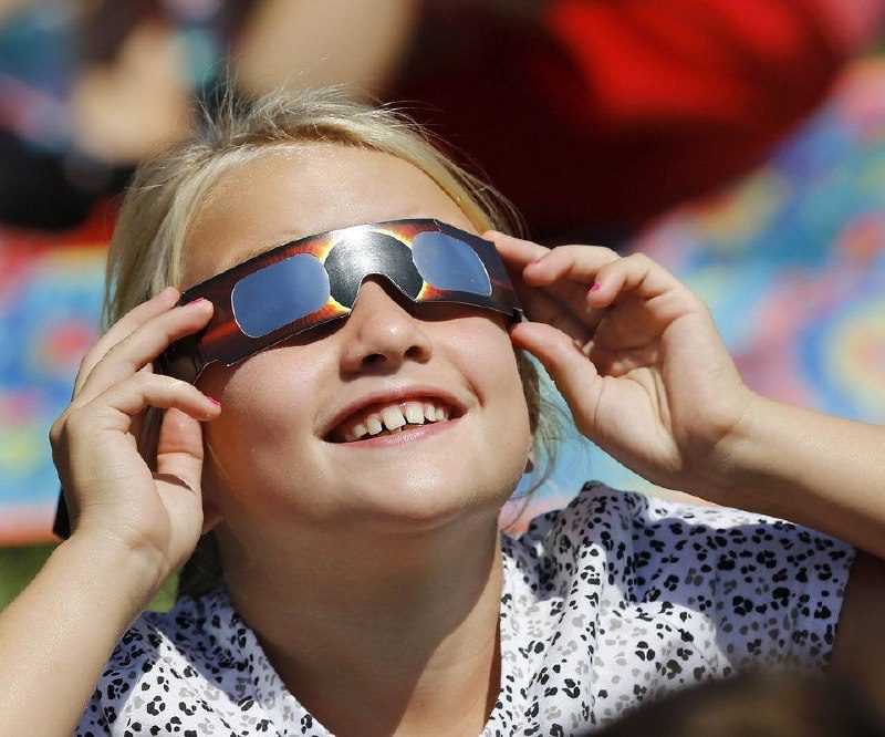 Smilende pige ser trygt op mod Solen gennem certificerede solformørkelsesbriller i klart dagslys.